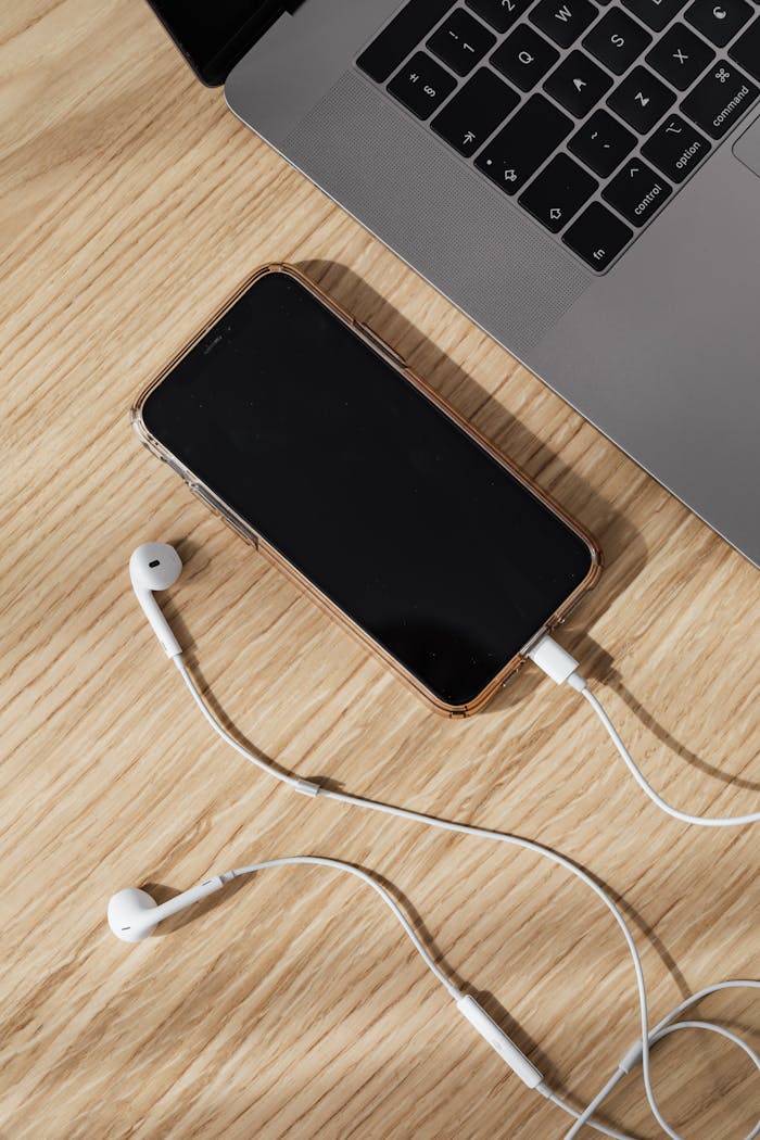 Modern workspace featuring a smartphone, laptop, and earphones on a wooden table.